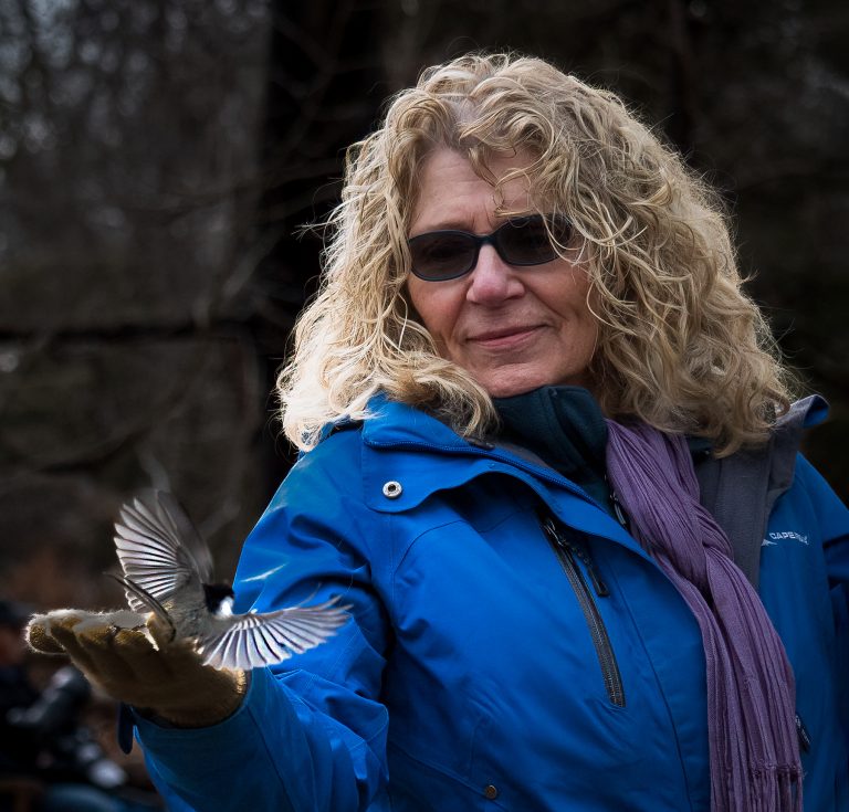 Woman extending her hand while a bird feeds out of it.